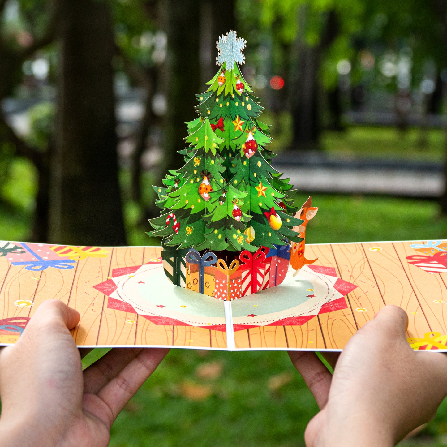 Hands holding a pop-up Christmas tree card with festive decorations.
