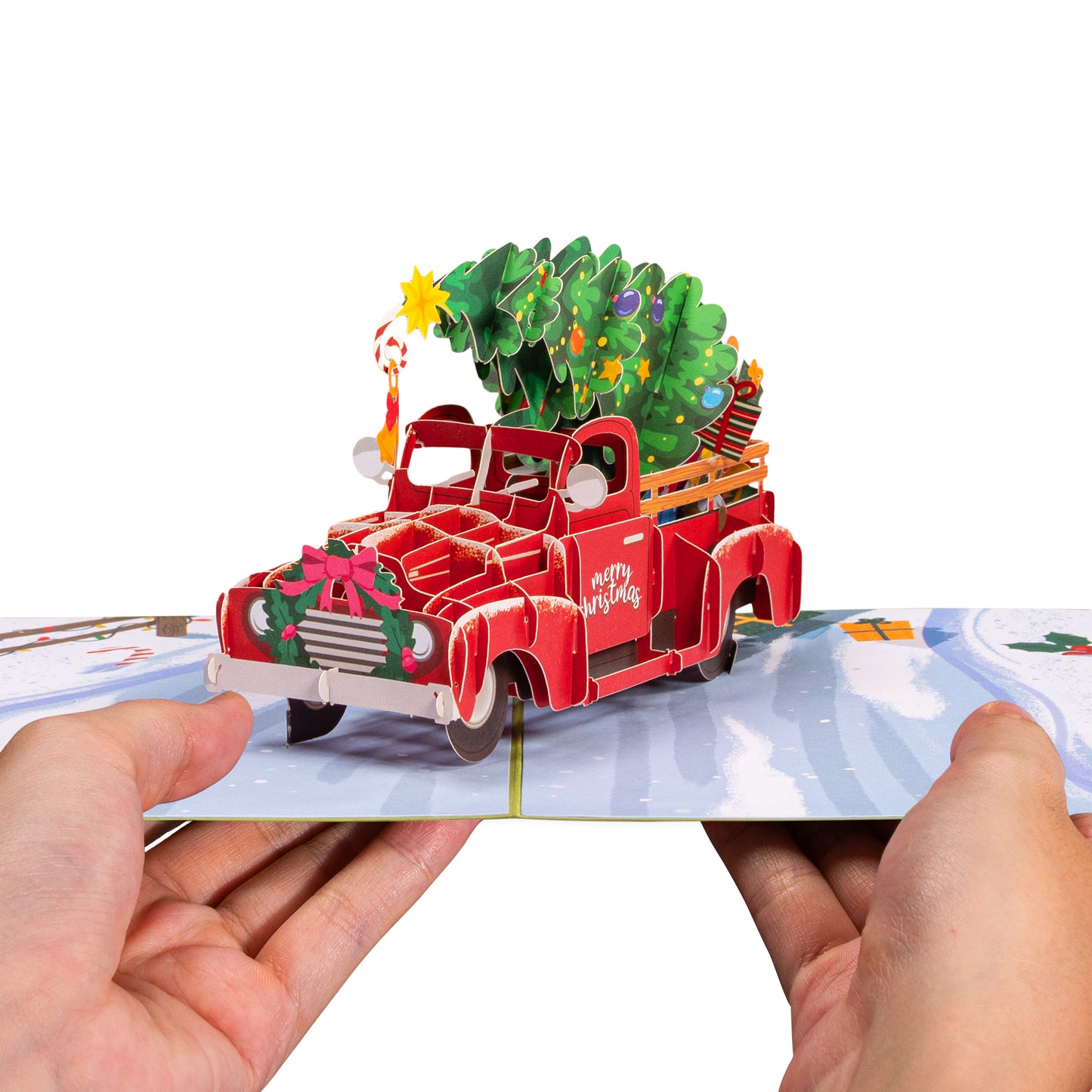 Hands holding a Christmas car pop-up card with a red truck and festive decorations.