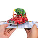 Hands holding a Christmas car pop-up card with a red truck and festive decorations.