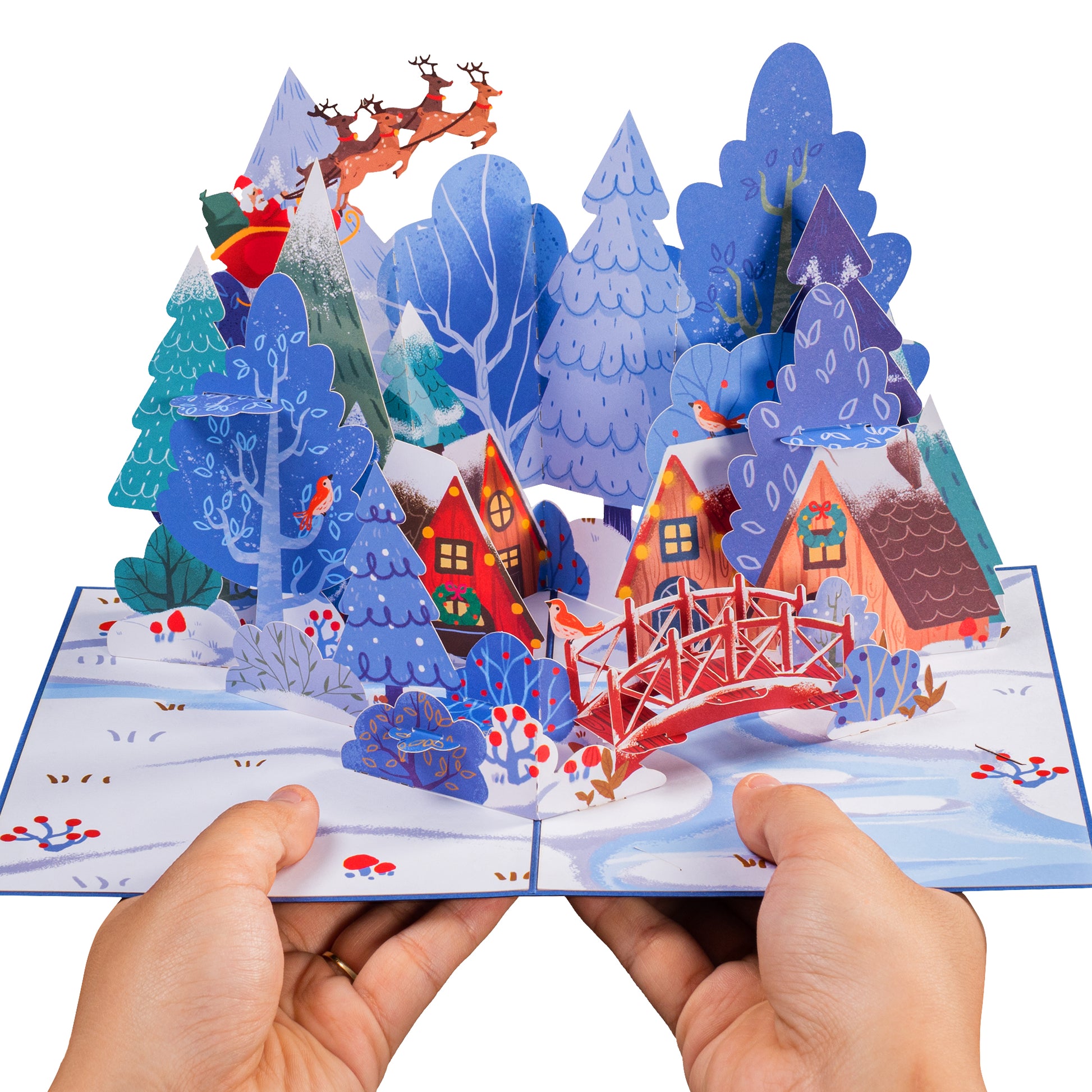 Hands holding the Magical Town Christmas pop-up card showcasing a festive winter village.