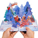 Hands holding the Magical Town Christmas pop-up card showcasing a festive winter village.