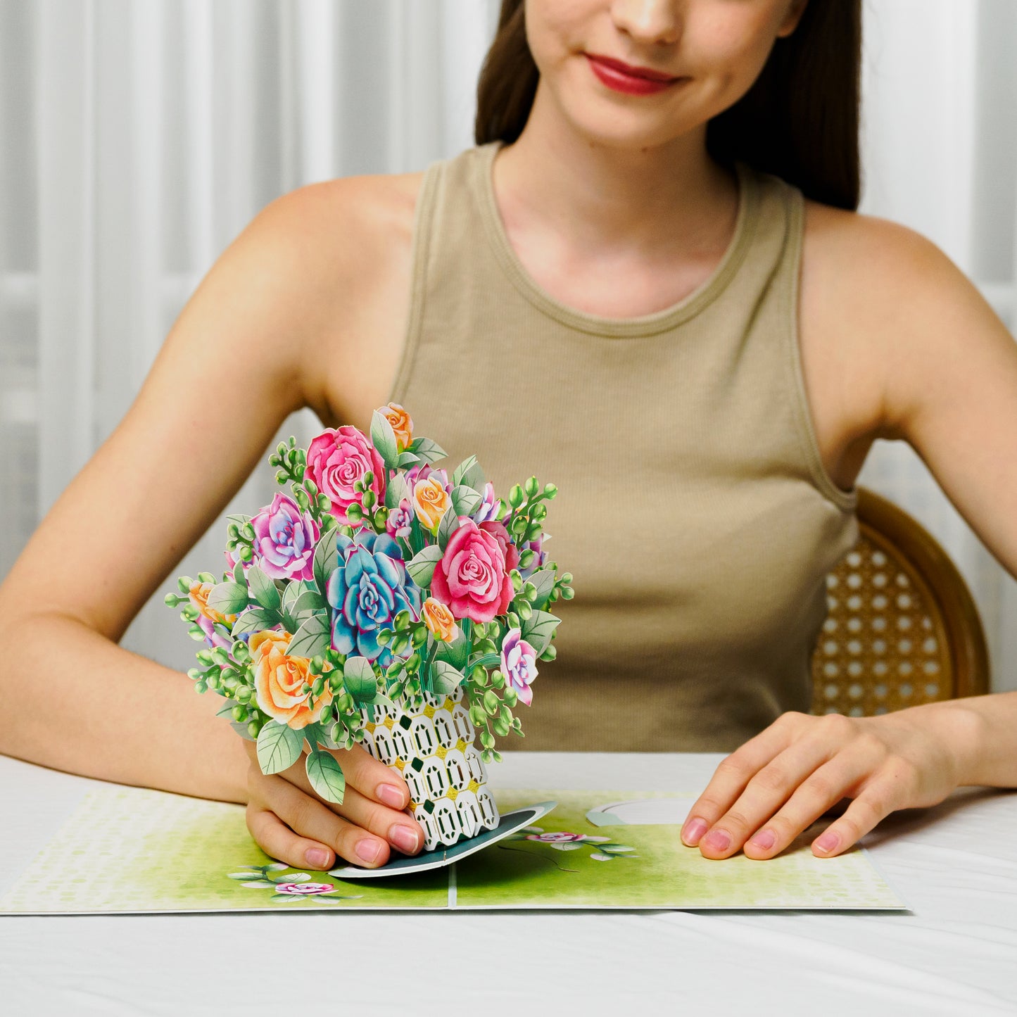 Person displaying a roses and succulent pop-up card on a table.