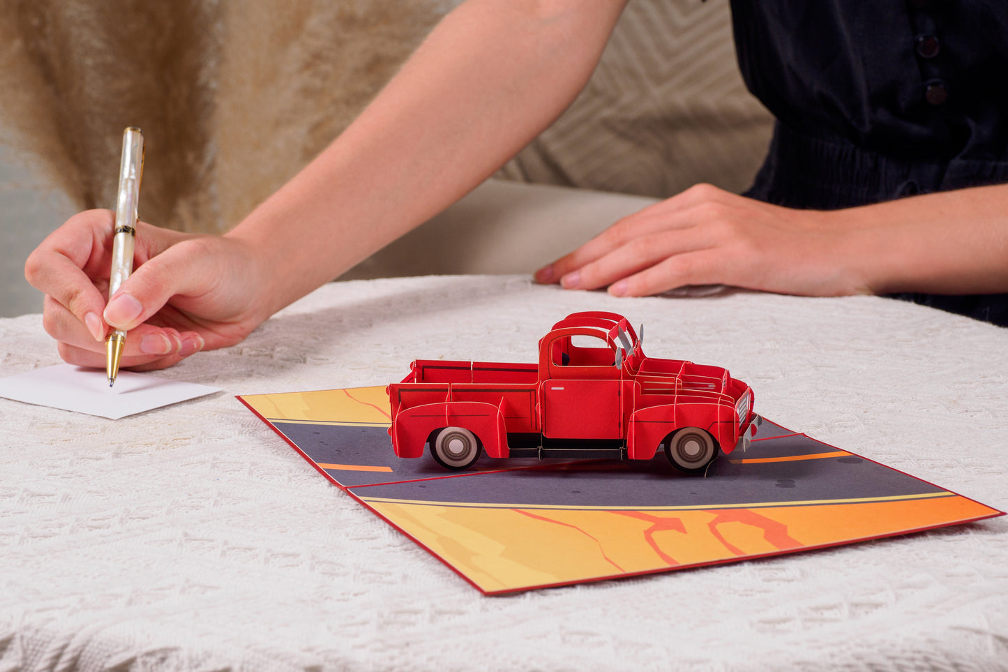 Person writing on an envelope next to the open Classic Truck Pop Up Card with a 3D red truck.