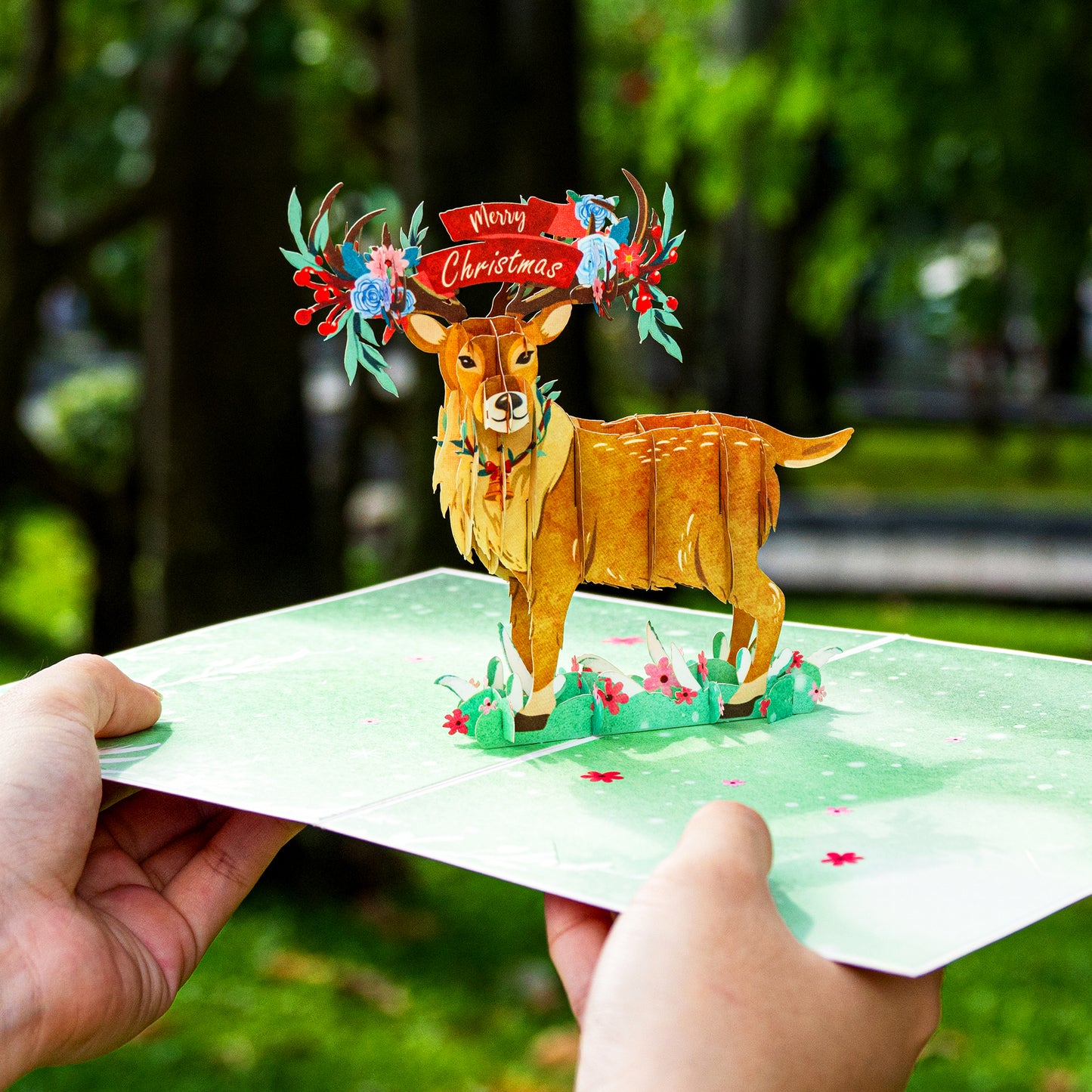 Hands holding a Christmas reindeer pop-up card with a 3D reindeer design.