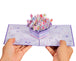 Hands holding a purple flowers pop-up card with intricate floral details.